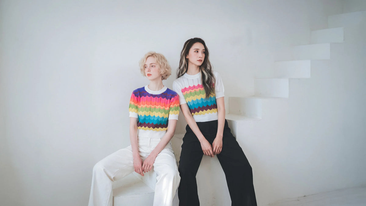 Two models wearing colourful short sleeve knit tops on white steps.