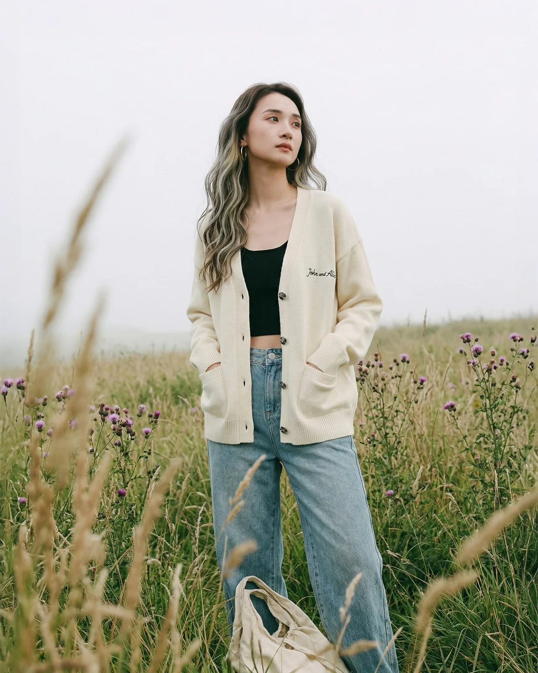 Collection card showing a woman standing in a grassy field wearing a cream cardigan over a black top and blue jeans.