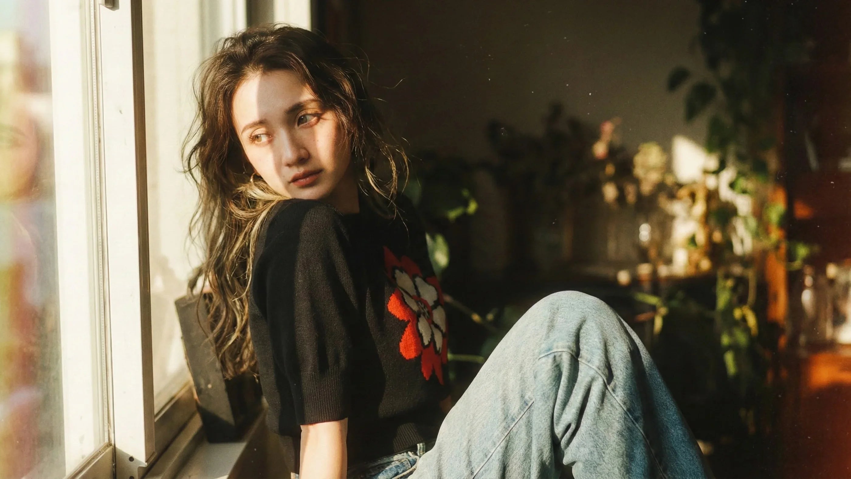 Featured piece banner showing a woman sitting by a sunlit window indoors, wearing a black short-sleeve knit top with a large red and red flower motif.