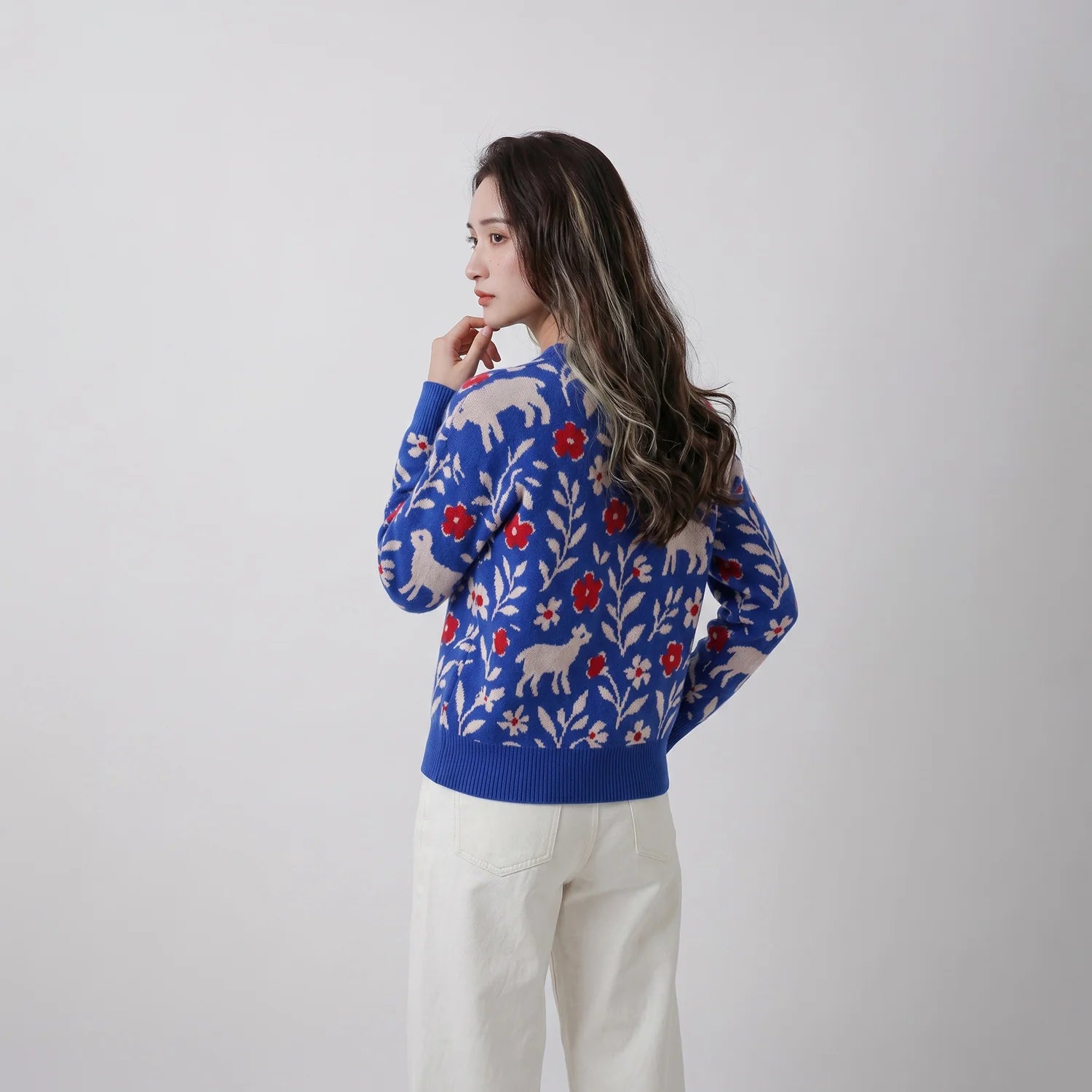 Back view of model wearing a blue merino wool jumper with sheep, flowers and foliage motifs.
