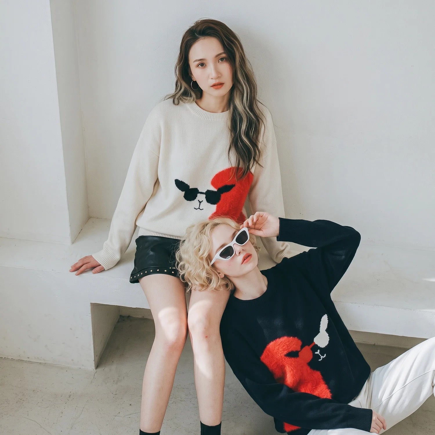 Two seated models wearing paired ivory and black jumpers with alpaca motifs.