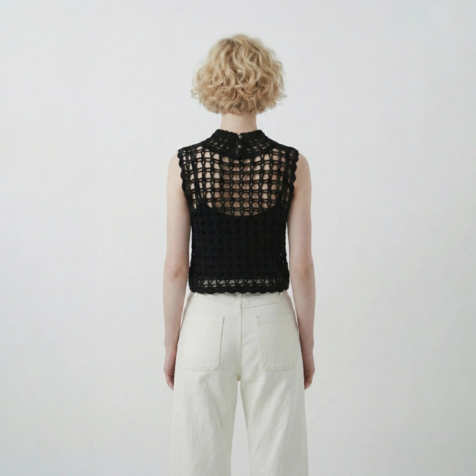 Back view of model wearing a black hand-crocheted sleeveless top with an open grid stitch and high neckline.
