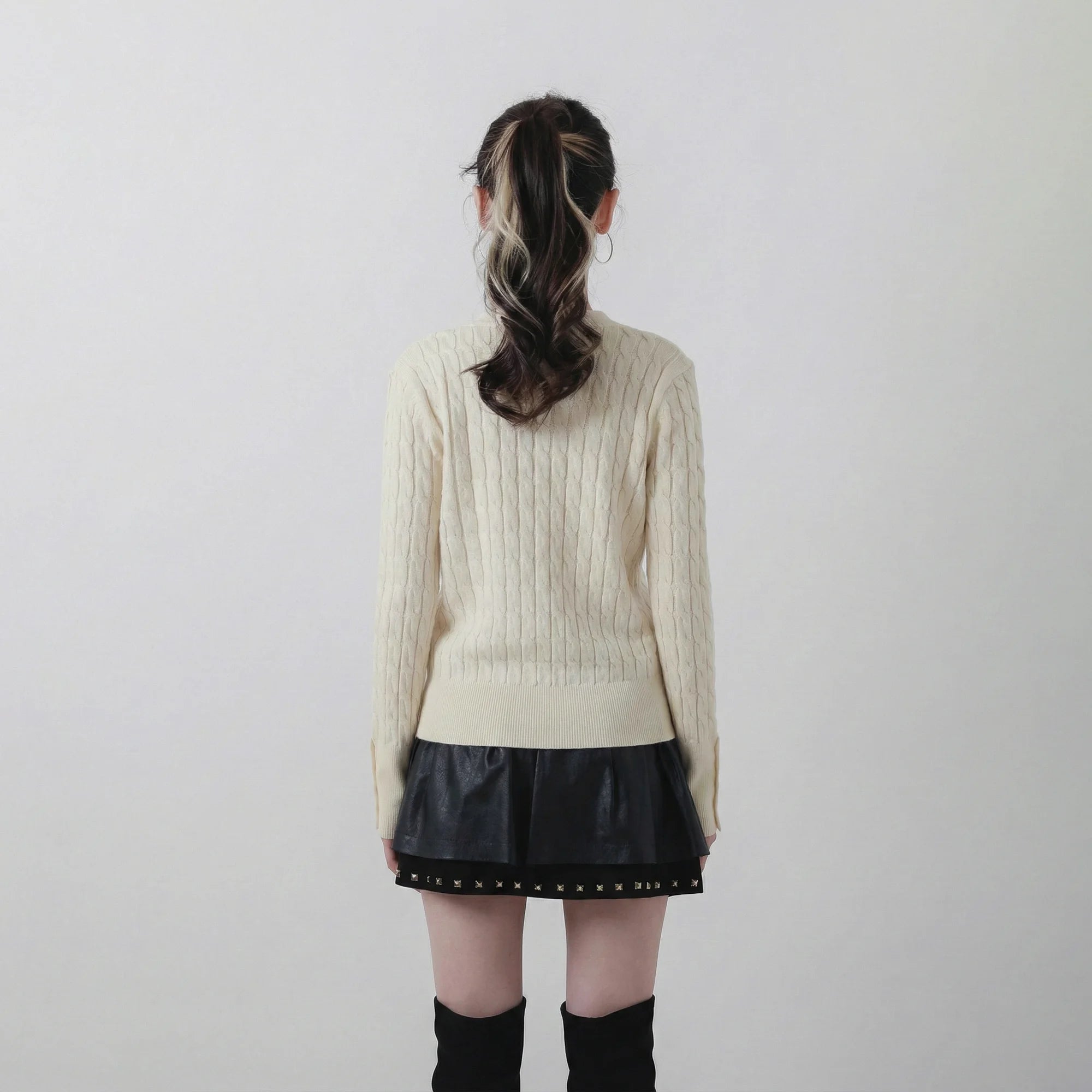 Back view of model wearing an ivory cable knit cardigan with all-over cable knit texture and a ribbed hem.