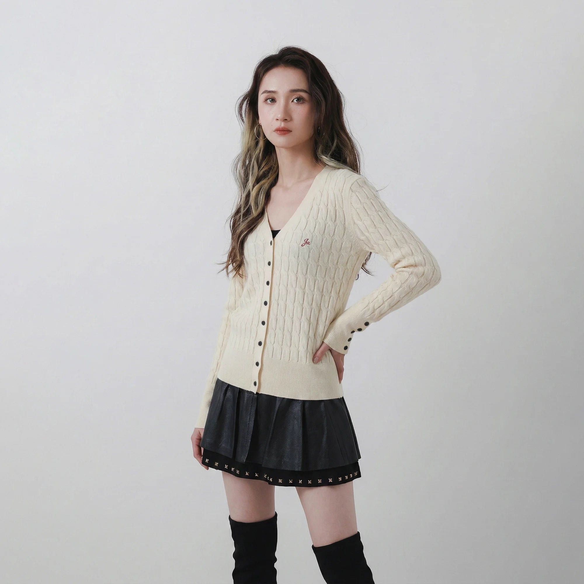 Model wearing an ivory cable knit cardigan with a V-neck, button front and cable knit texture.