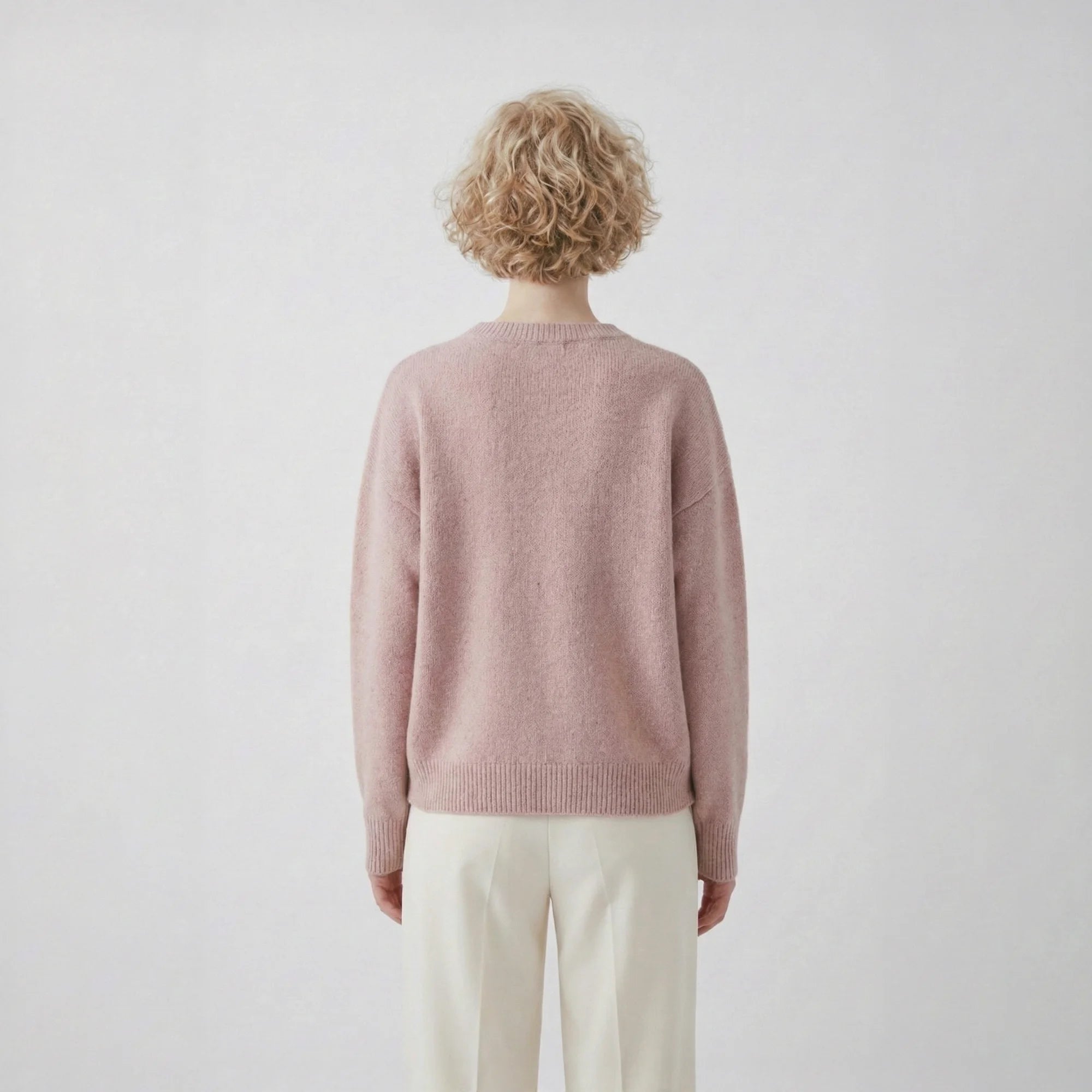 Back view of model wearing a blush pink jumper with a slightly oversized silhouette and ribbed hem.