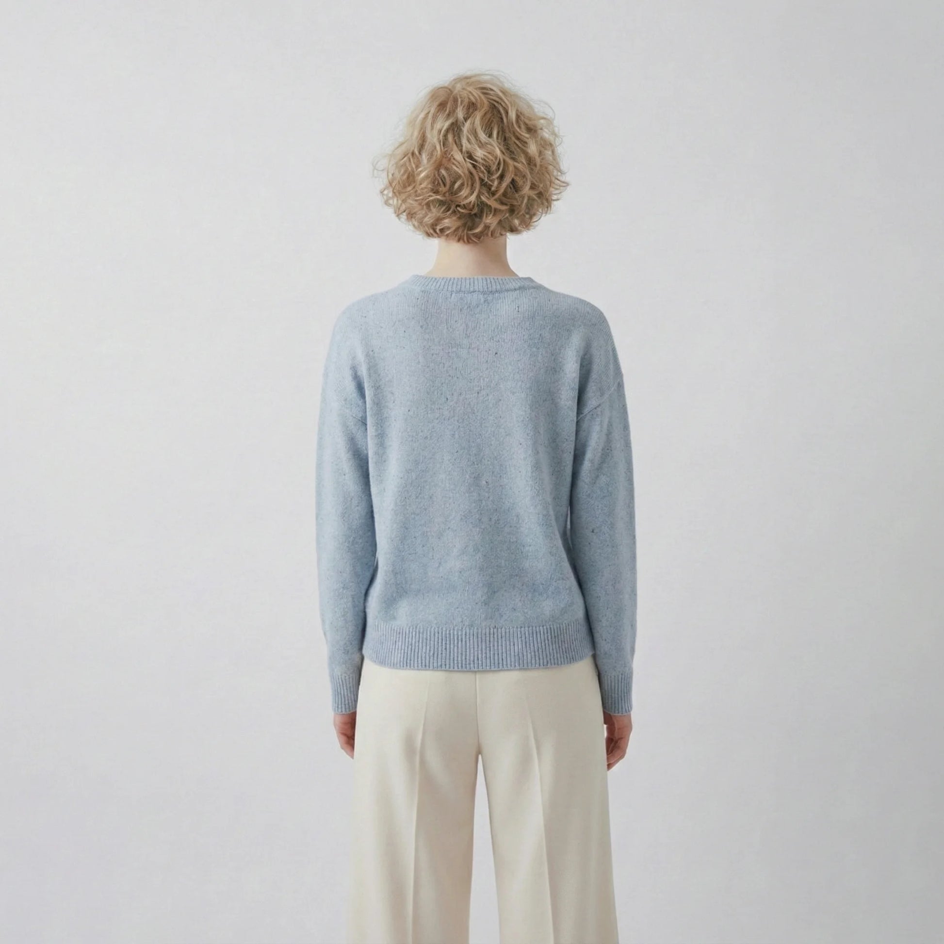 Back view of model wearing a light blue jumper with a slightly oversized silhouette and ribbed hem.