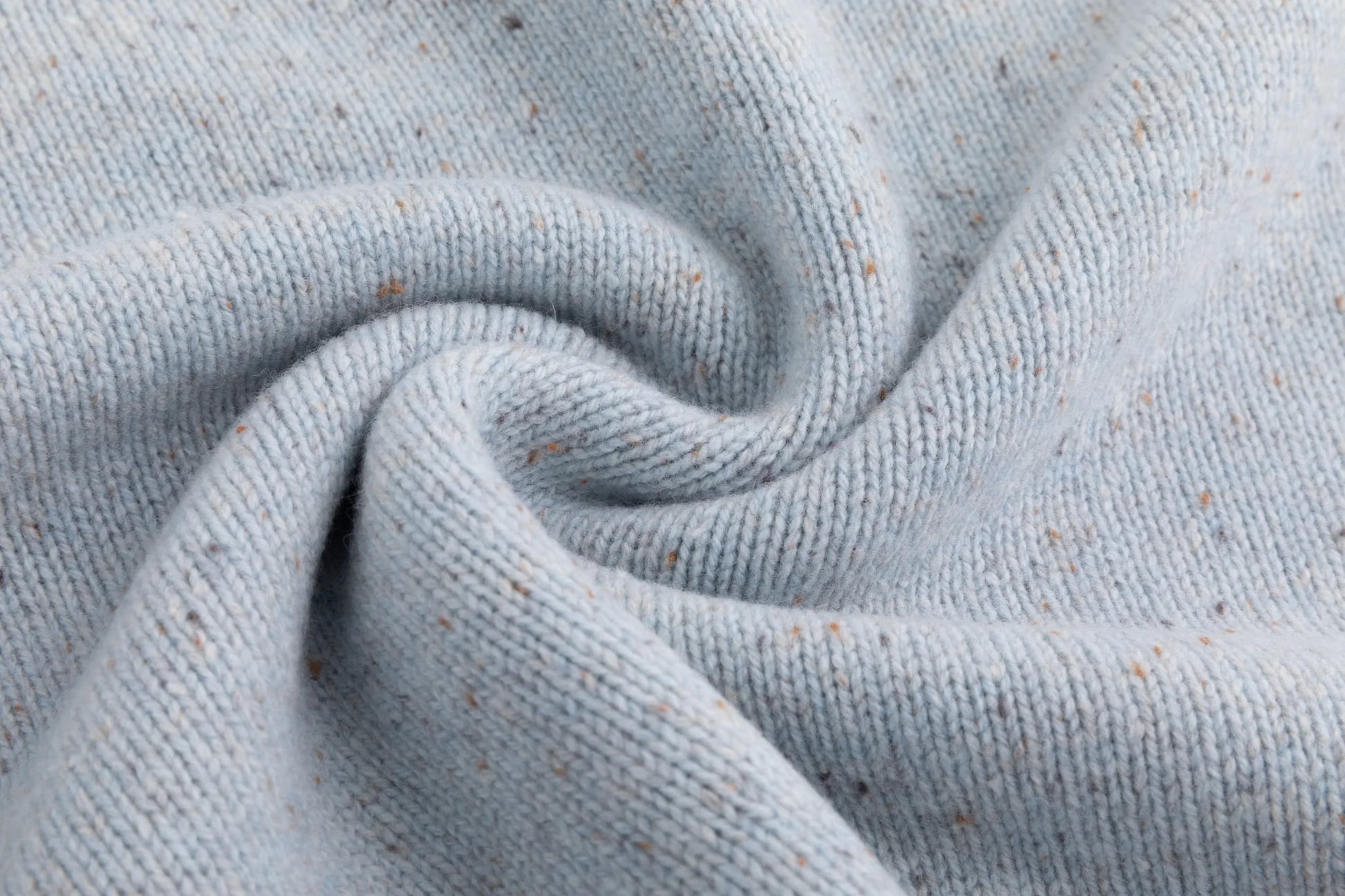 Close-up of the fine speckled knit texture on the light blue jumper.
