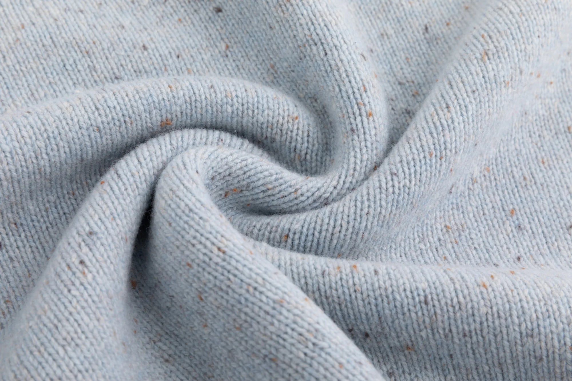 Close-up of the fine speckled knit texture on the light blue jumper.
