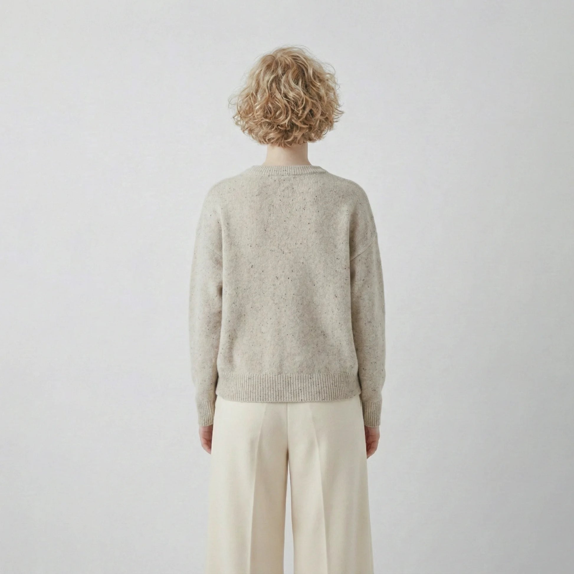 Back view of model wearing an oatmeal jumper with a slightly oversized silhouette and ribbed hem.