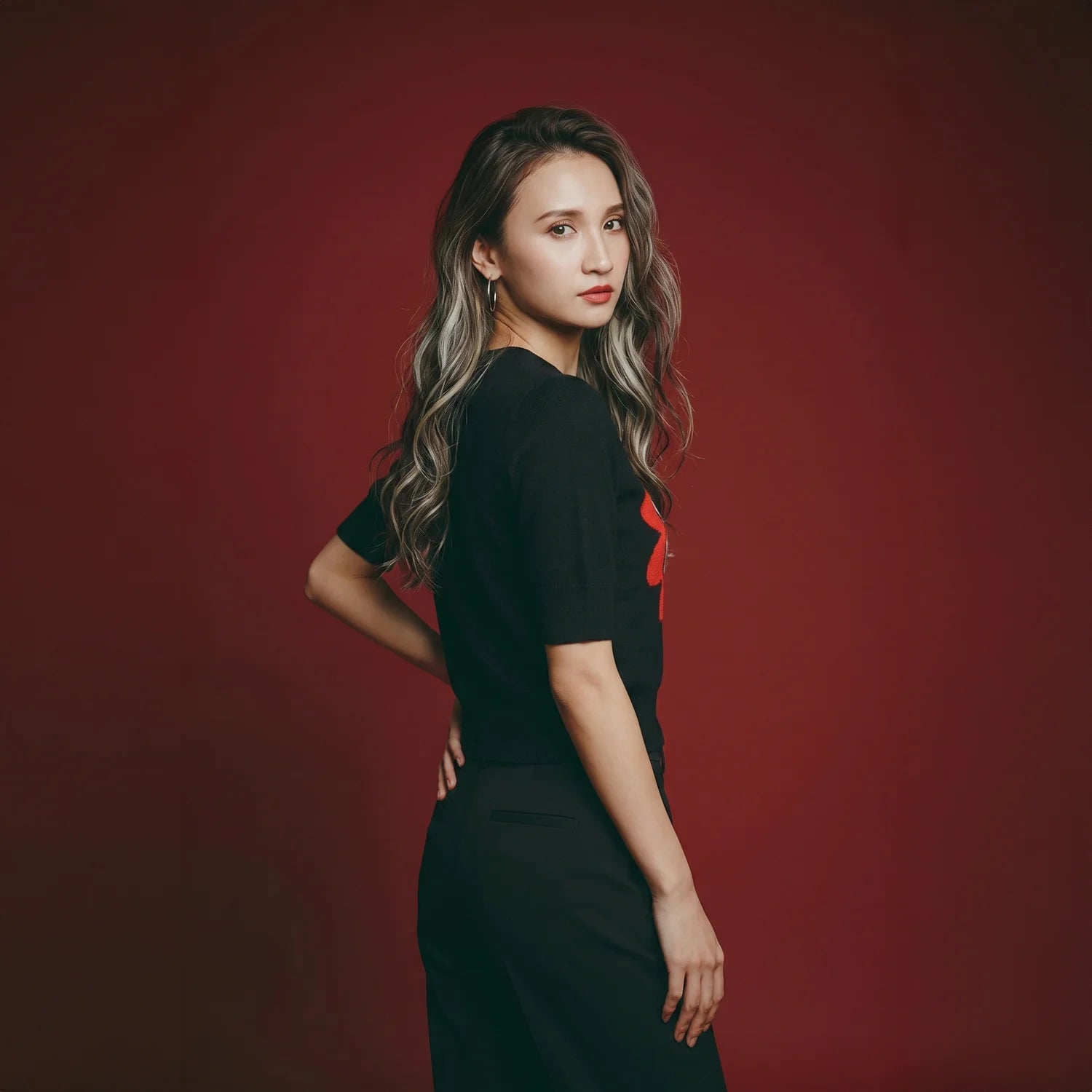 Rear view of model wearing a black knit top with part of the red flower motif visible.