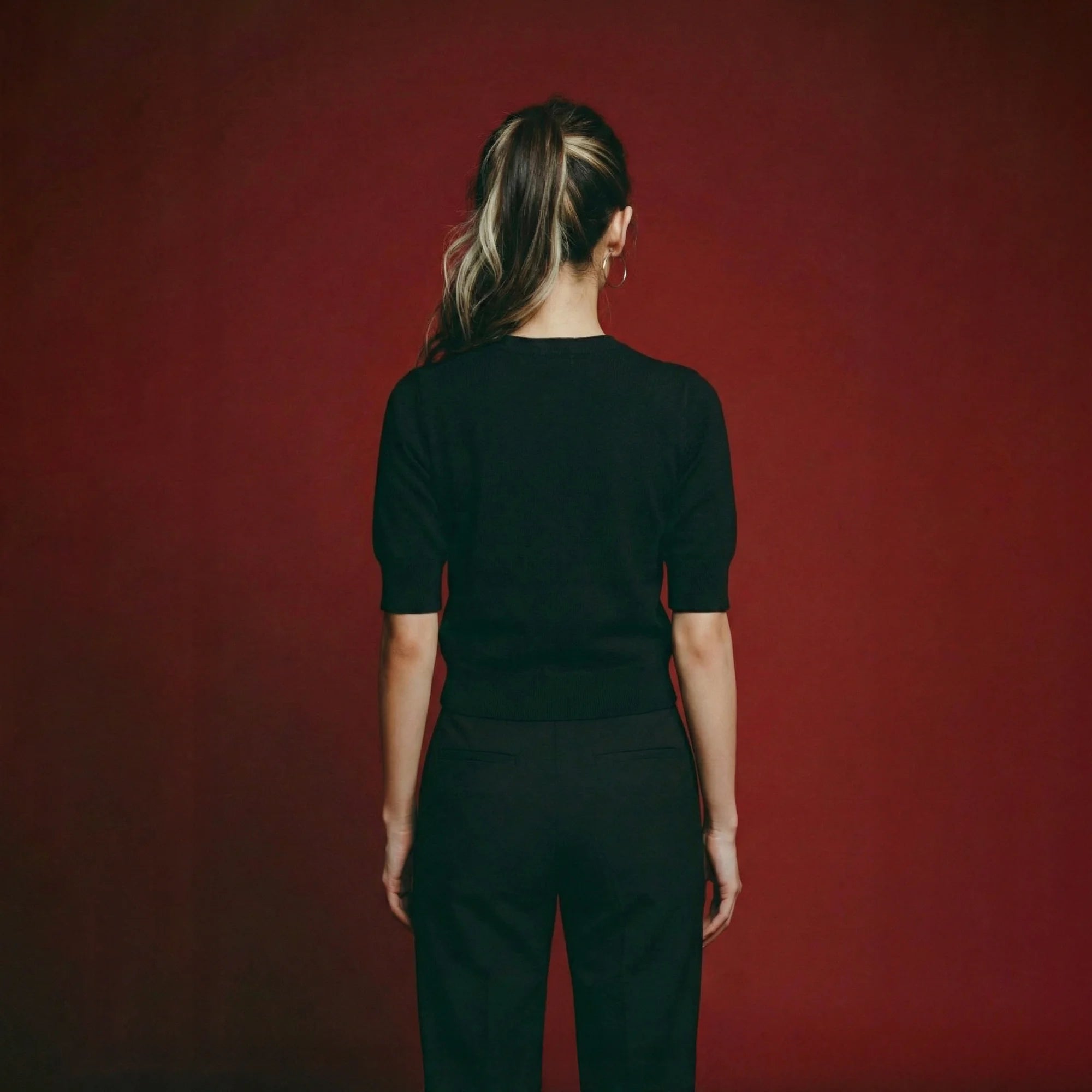 Back view of model wearing a black short-sleeve knit top with a plain back.