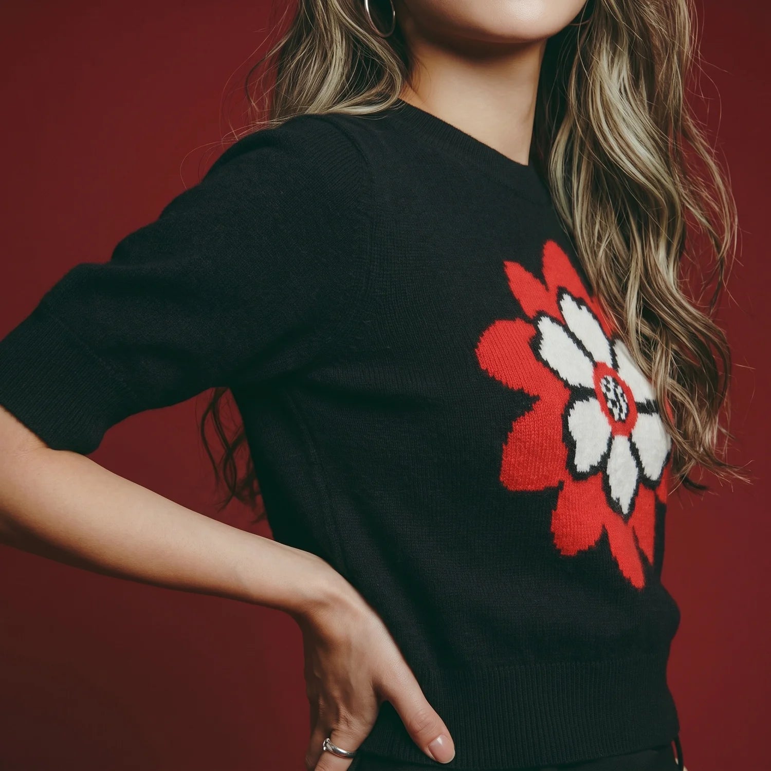 Close-up of model wearing a black short-sleeve knit top with a red and white flower motif.