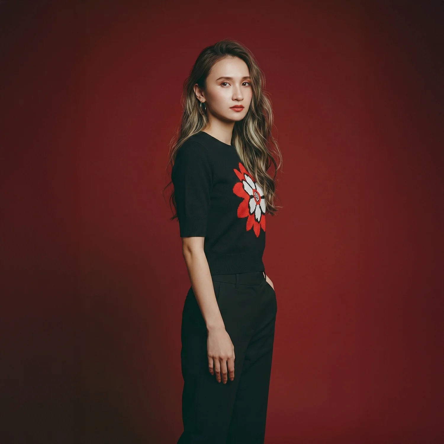 Model wearing a black knit top with a red and white flower motif.