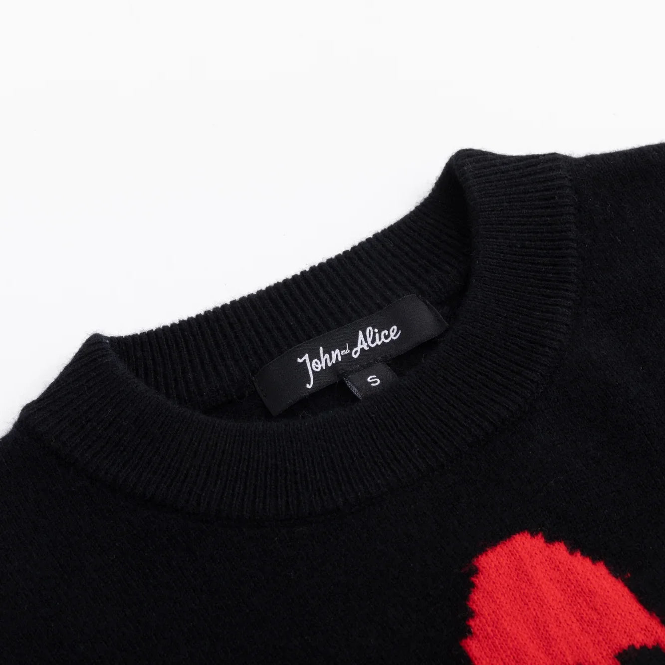 Close-up of the ribbed neckline and John and Alice label on the black knit top.