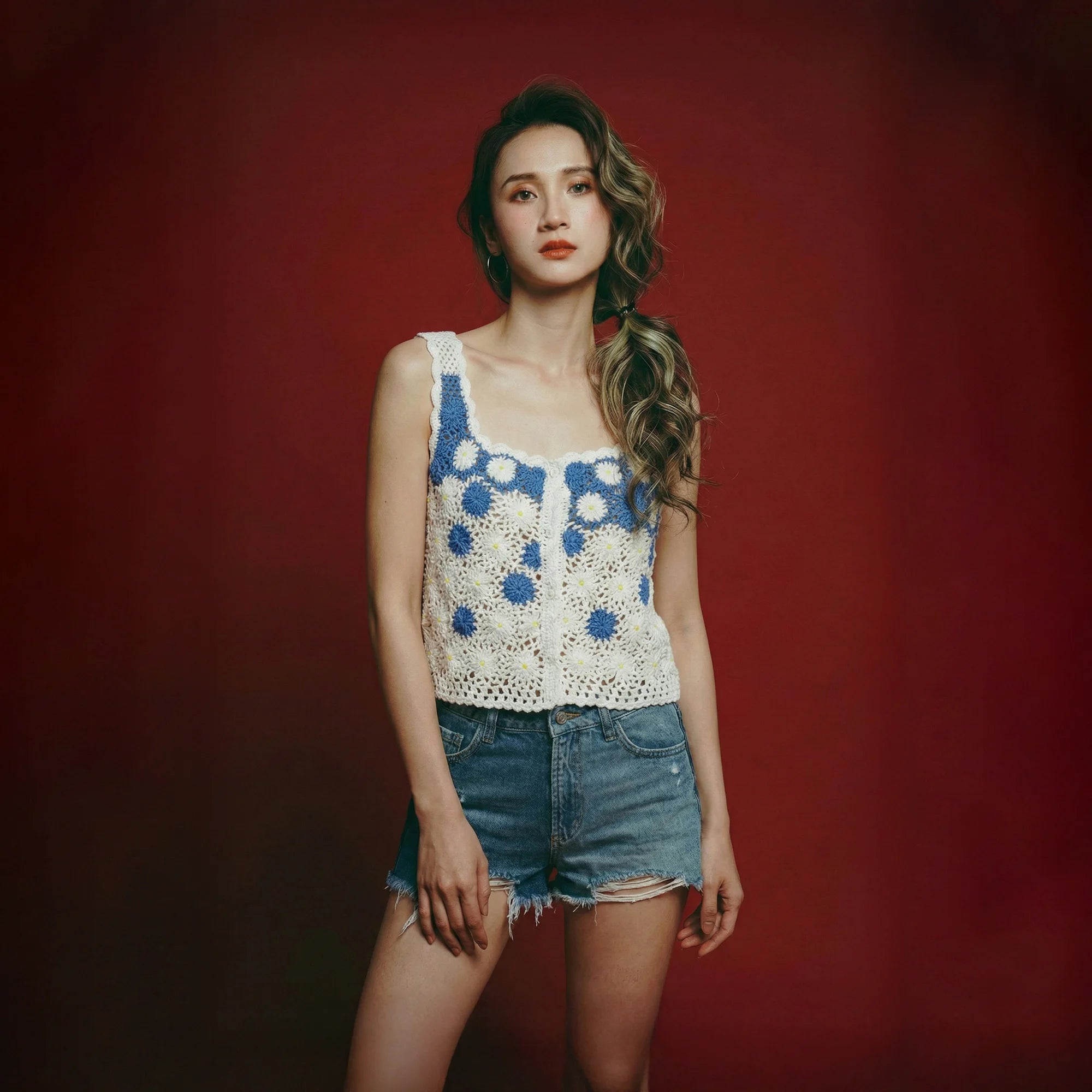 Model wearing a blue and white crochet camisole top with floral motifs and scalloped straps.