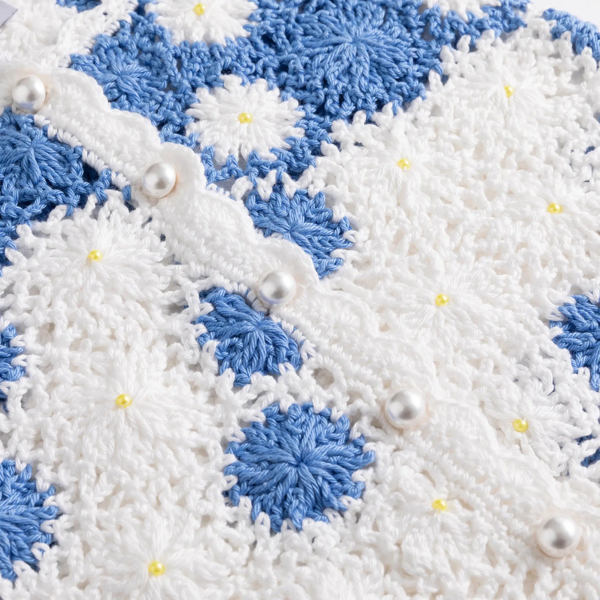 Close-up of the crochet flowers and small bead details on the white and blue top.