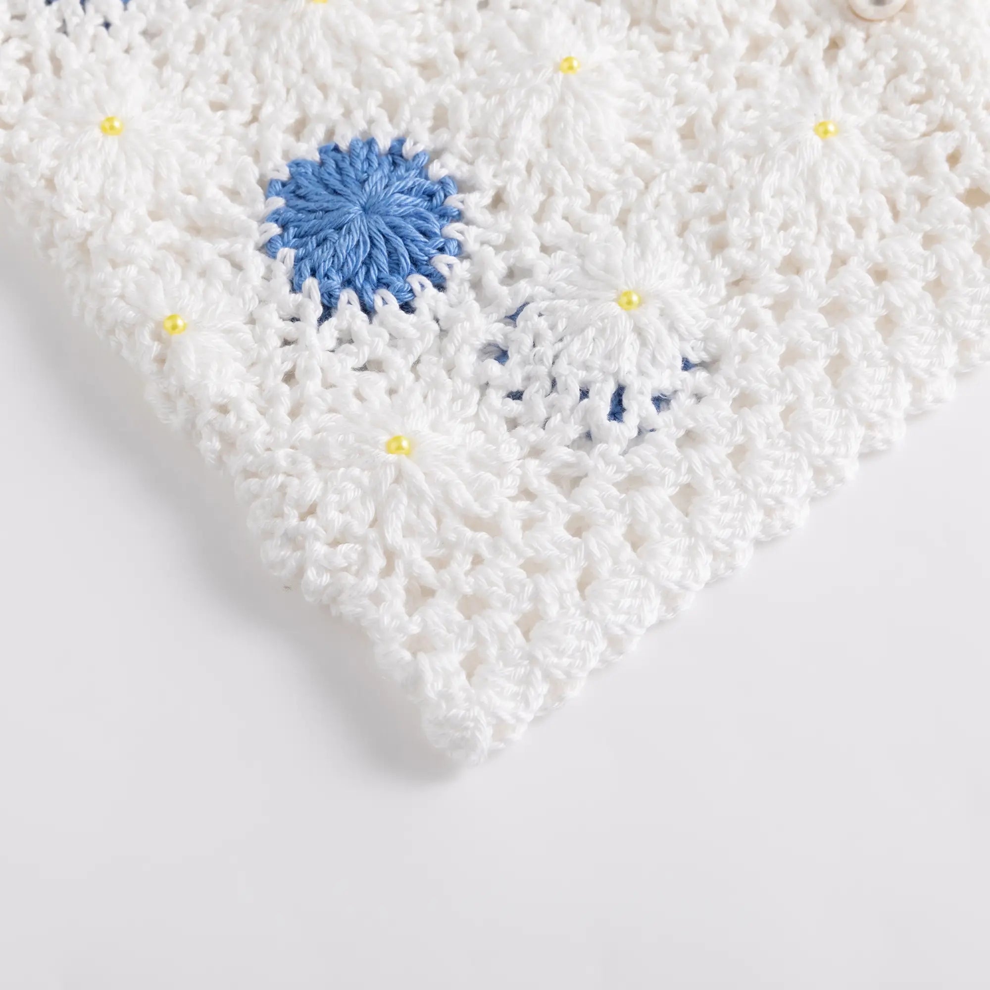 Close-up of the lower corner of the crochet top showing the blue floral motif and bead detail.