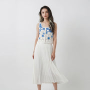 Model wearing a hand-crocheted fitted top in white and blue with floral motifs and small bead details, paired with a white pleated skirt.