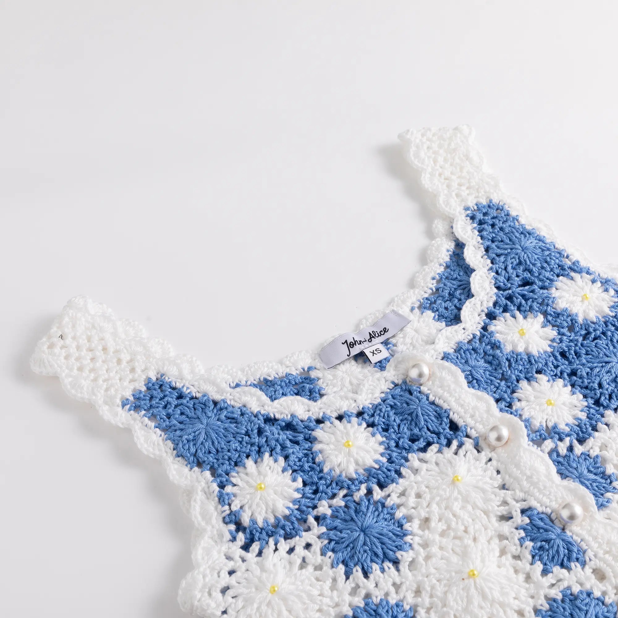 Close-up of the scoop neckline and shoulder strap on the white crochet top with blue floral motifs.