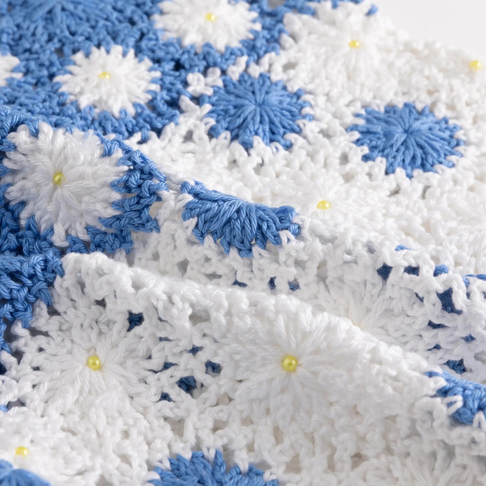 Close-up of the open crochet texture with blue floral motifs and small bead details.