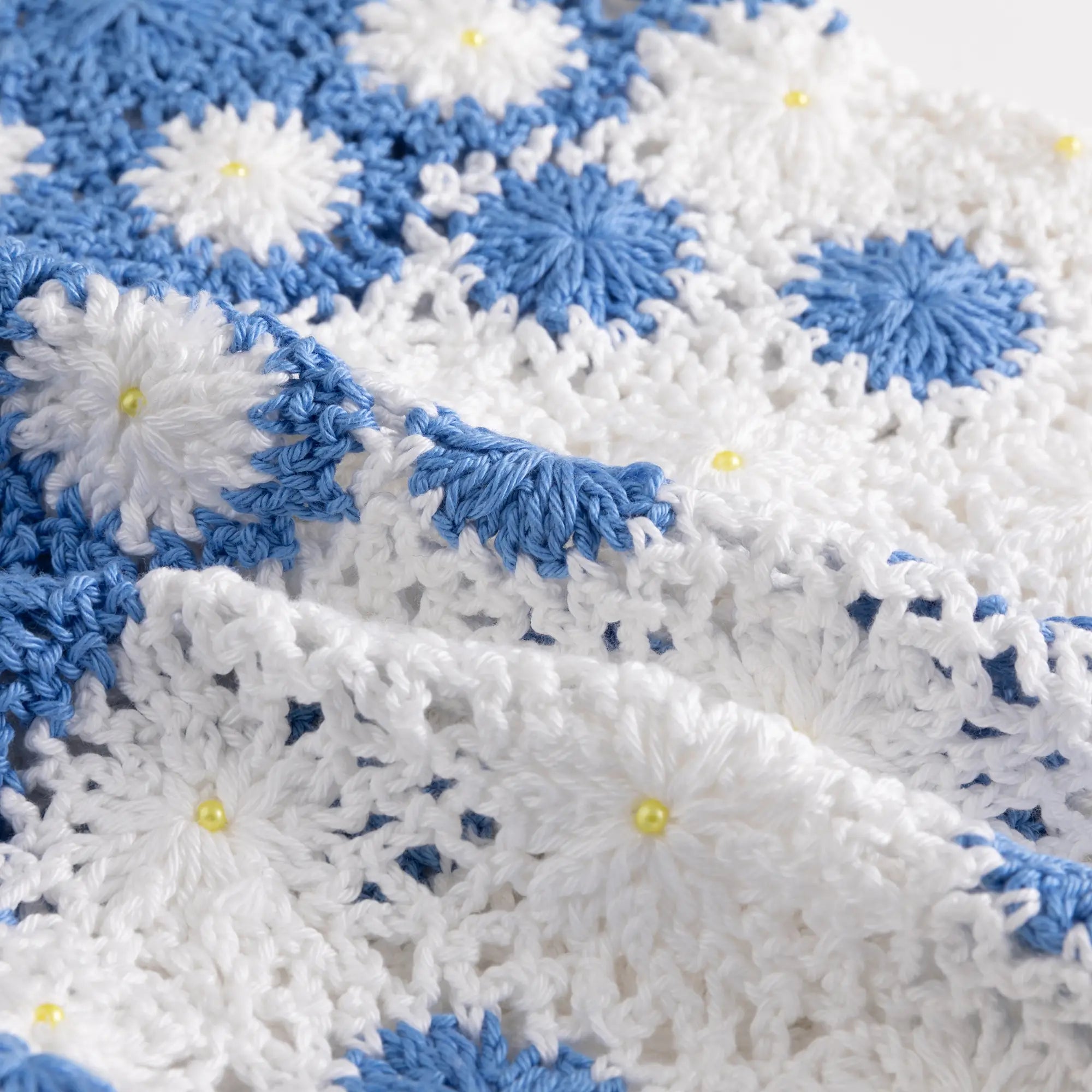 Close-up of the open crochet texture with blue floral motifs and small bead details.