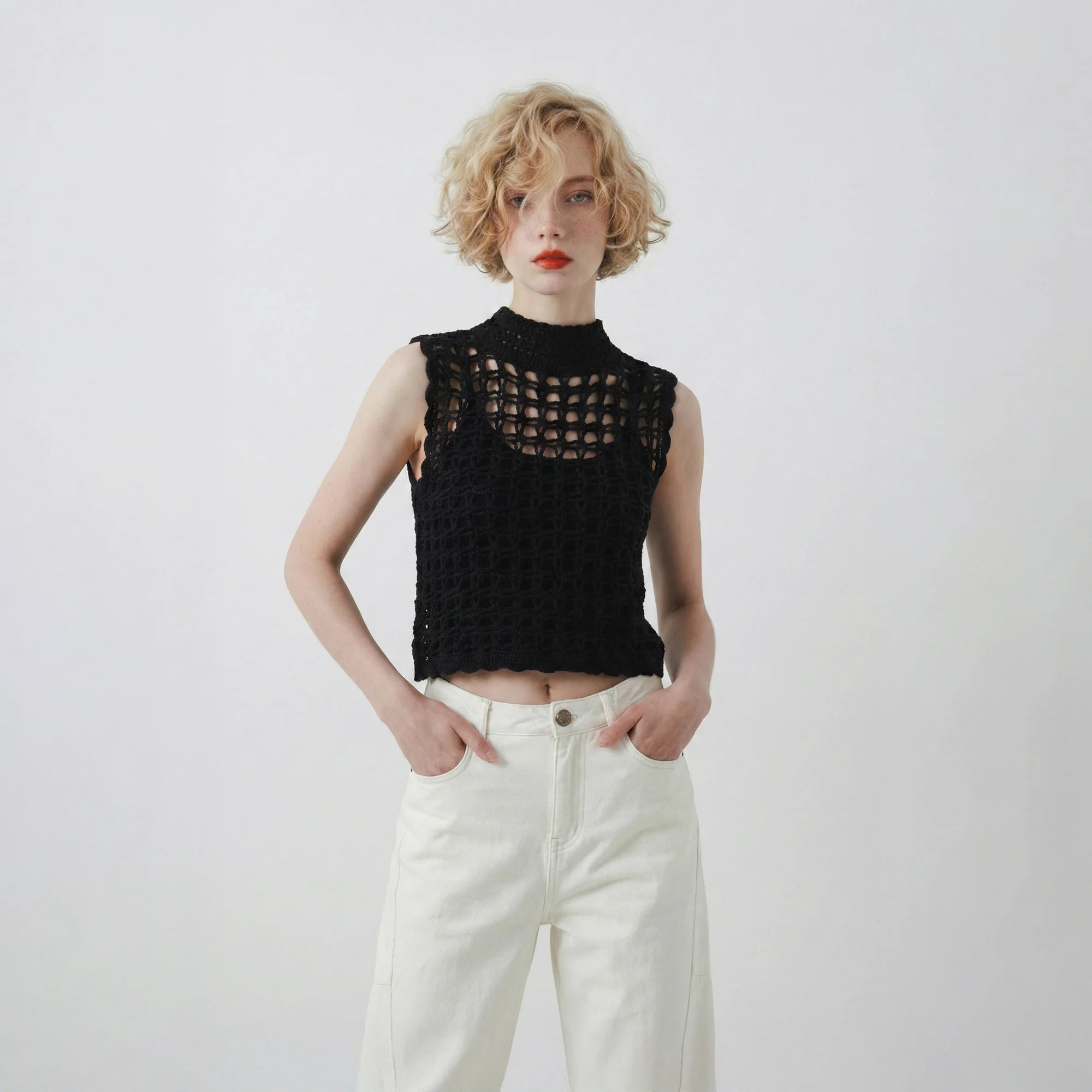 Model wearing a black hand-crocheted sleeveless top with a high neckline and open grid stitch.