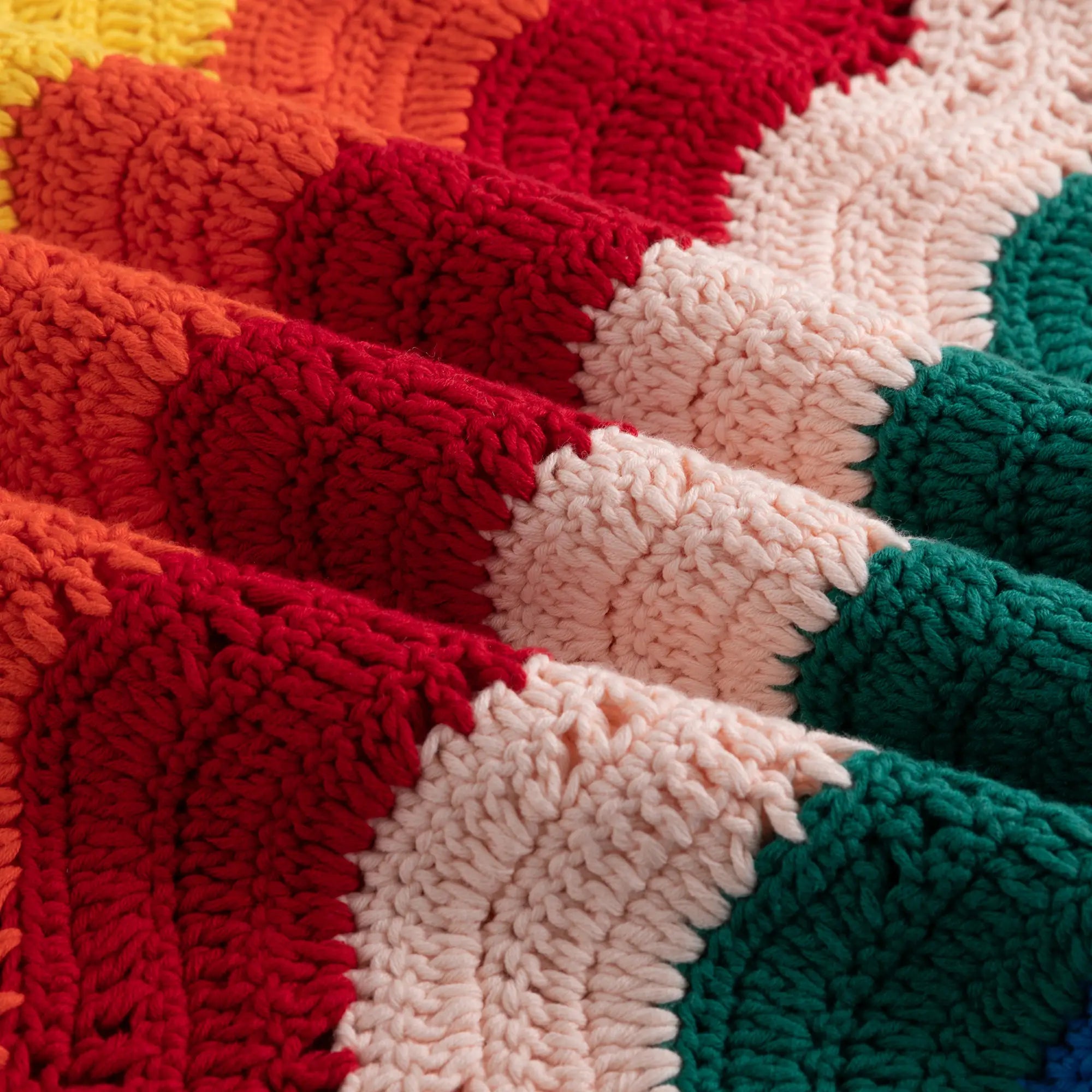 Close-up of a multicoloured crochet knit texture with raised loop stitches in red, orange, cream, teal, green, and blue.