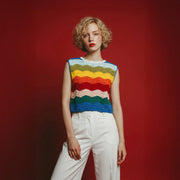 Model wearing a hand-crocheted relaxed top with multicolour wave stripes, paired with white trousers.
