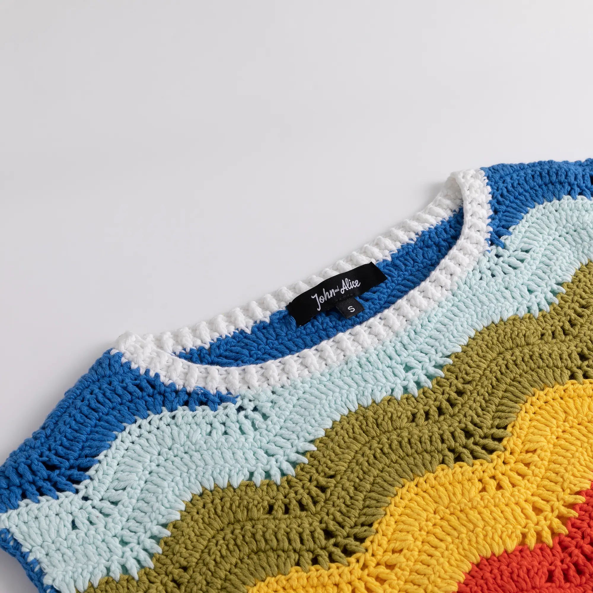 Close-up of the round neckline and upper front of the crochet top with multicolour wave stripes.