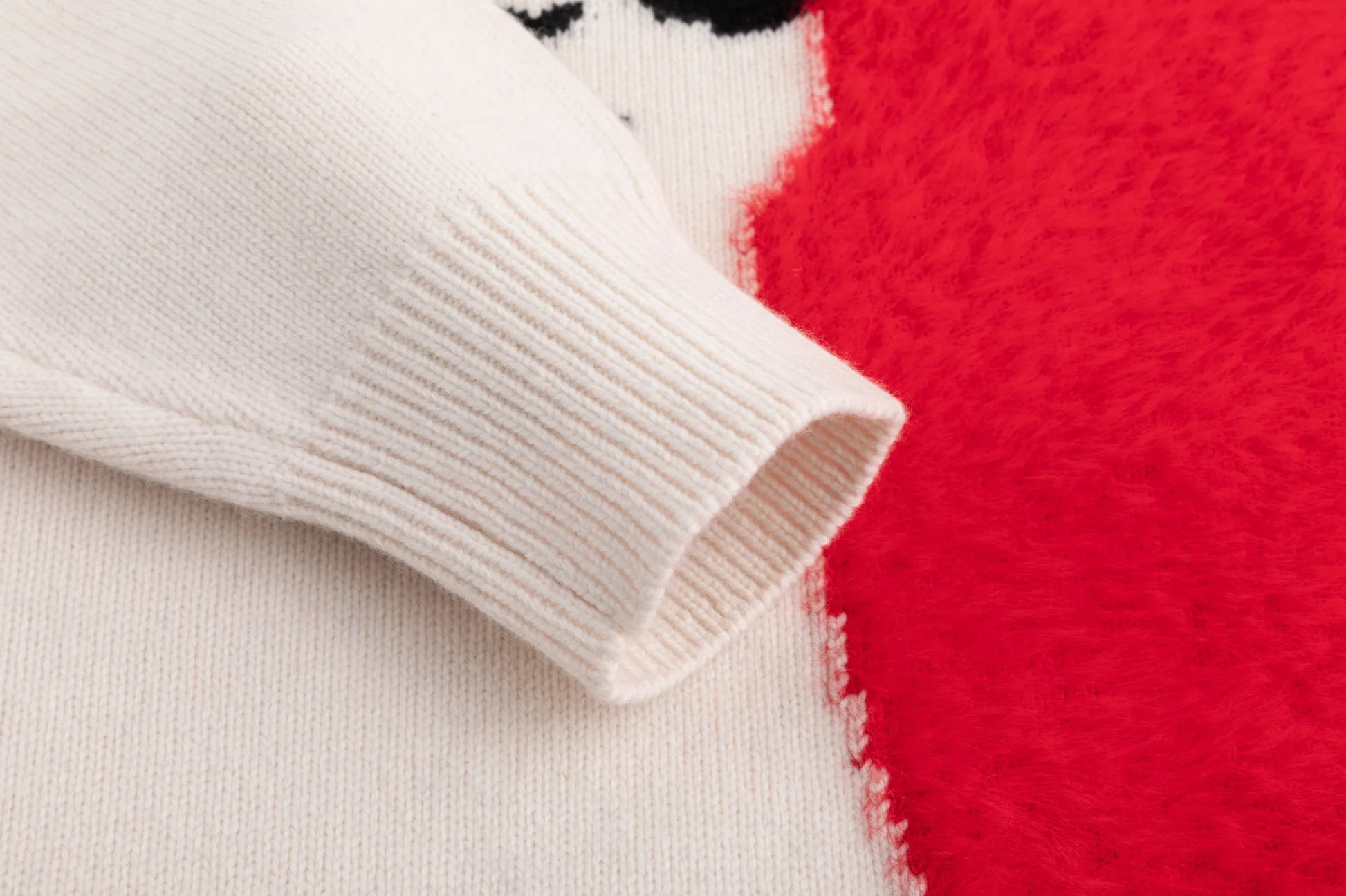 Close-up of the ribbed cuff and fuzzy heart panel on the cream jumper.