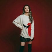 Model wearing a cream oversized intarsia jumper with a llama face motif, black sunglasses and a bright red fuzzy heart panel.