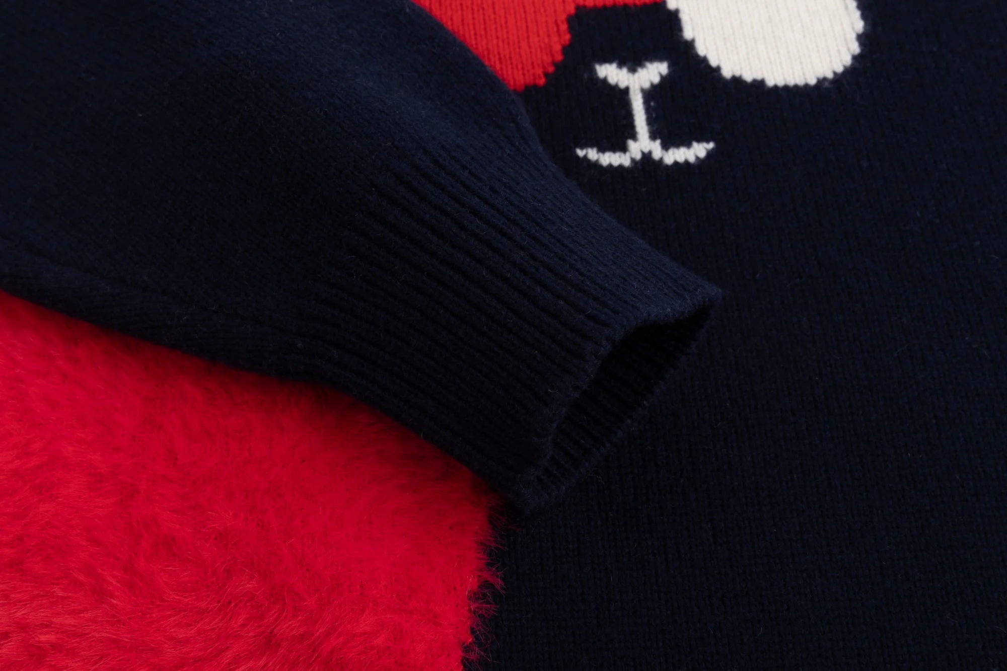 Close-up of the ribbed cuff and bright red fuzzy heart panel on the navy jumper.