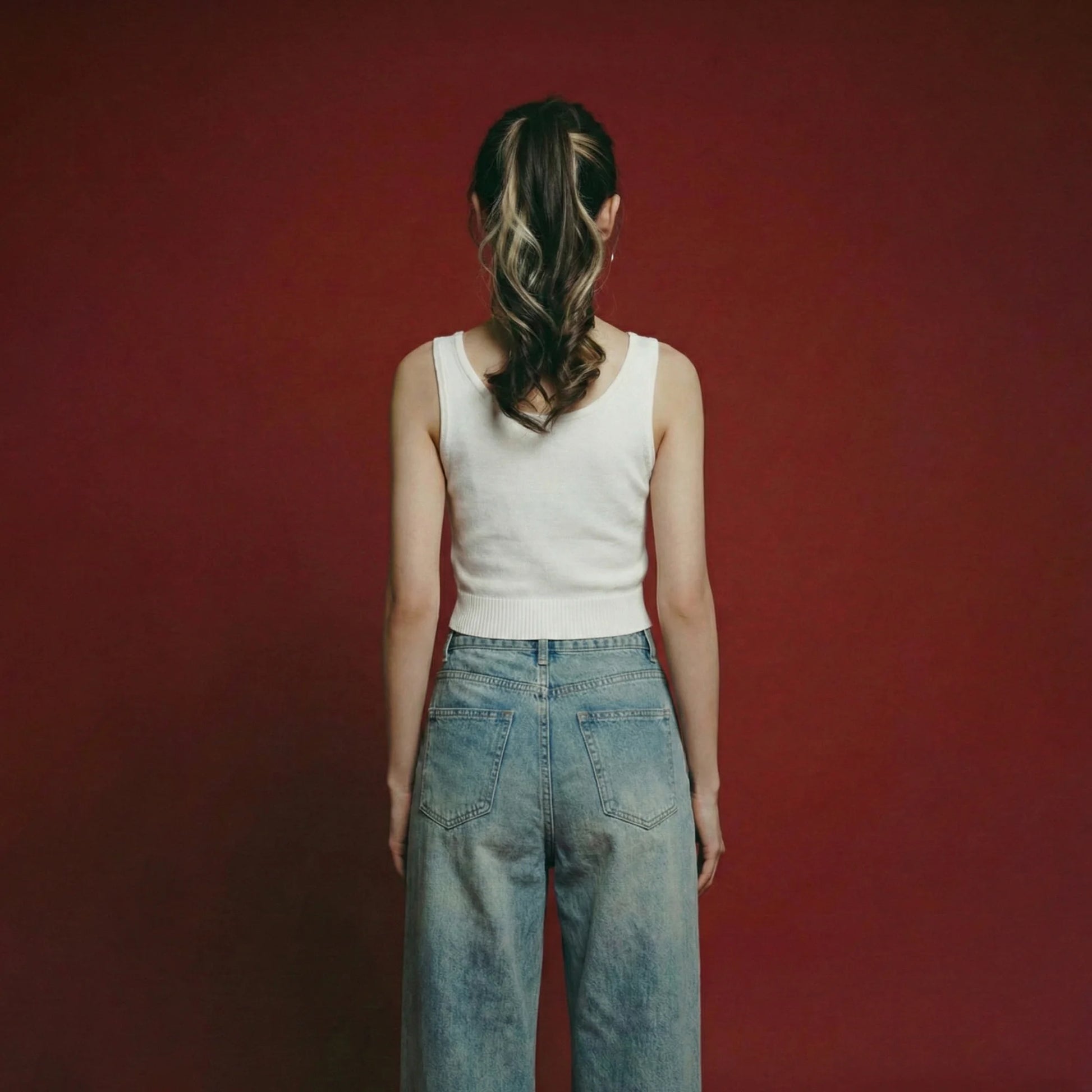 Back view of woman wearing an ivory knit tank with a scoop neckline and ribbed hem.