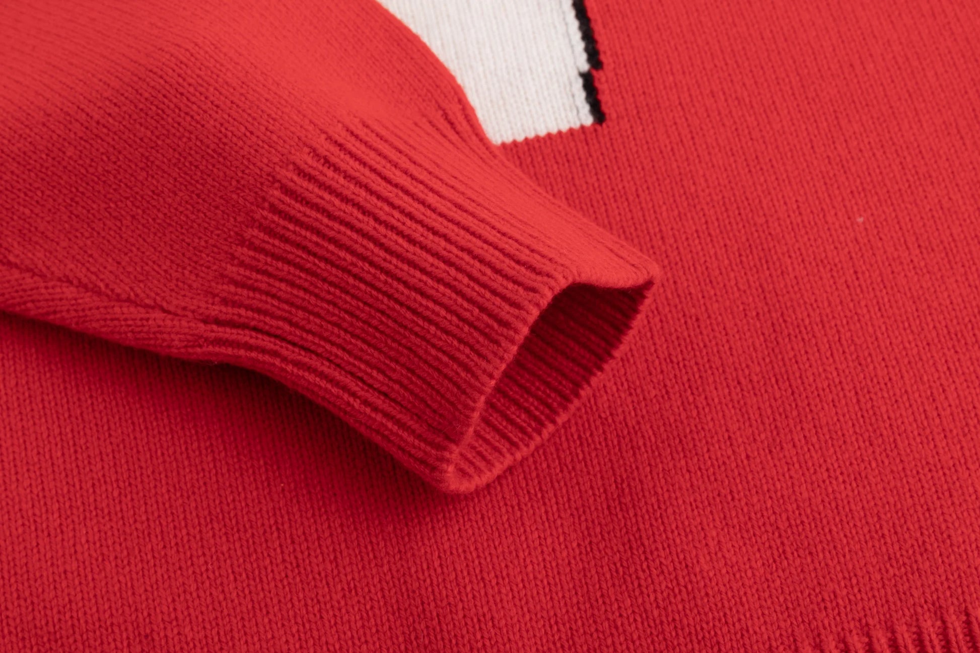 Close-up of a bright red knit jumper showing the ribbed sleeve cuff and soft, fine-gauge texture.