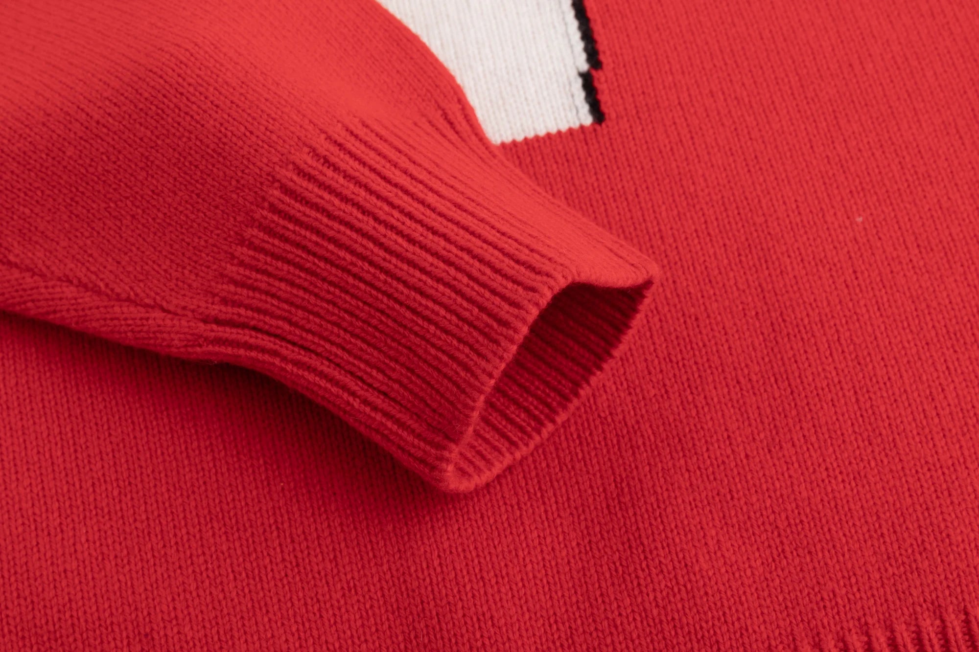Close-up of a bright red knit jumper showing the ribbed sleeve cuff and soft, fine-gauge texture.