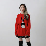Model wearing a red wool blend jumper with an oversized fit and an abstract rabbit jacquard with a black velvet bow on the front.