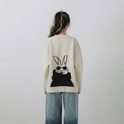 Back view of model wearing an ivory merino wool cardigan with a rabbit jacquard in sunglasses and a black feather yarn cape.