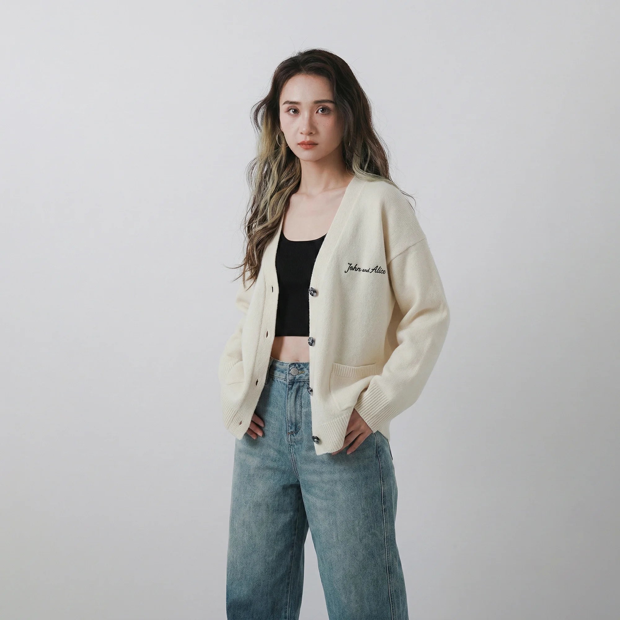 Model wearing an ivory merino wool cardigan with an oversized fit, V-neck and front patch pockets.