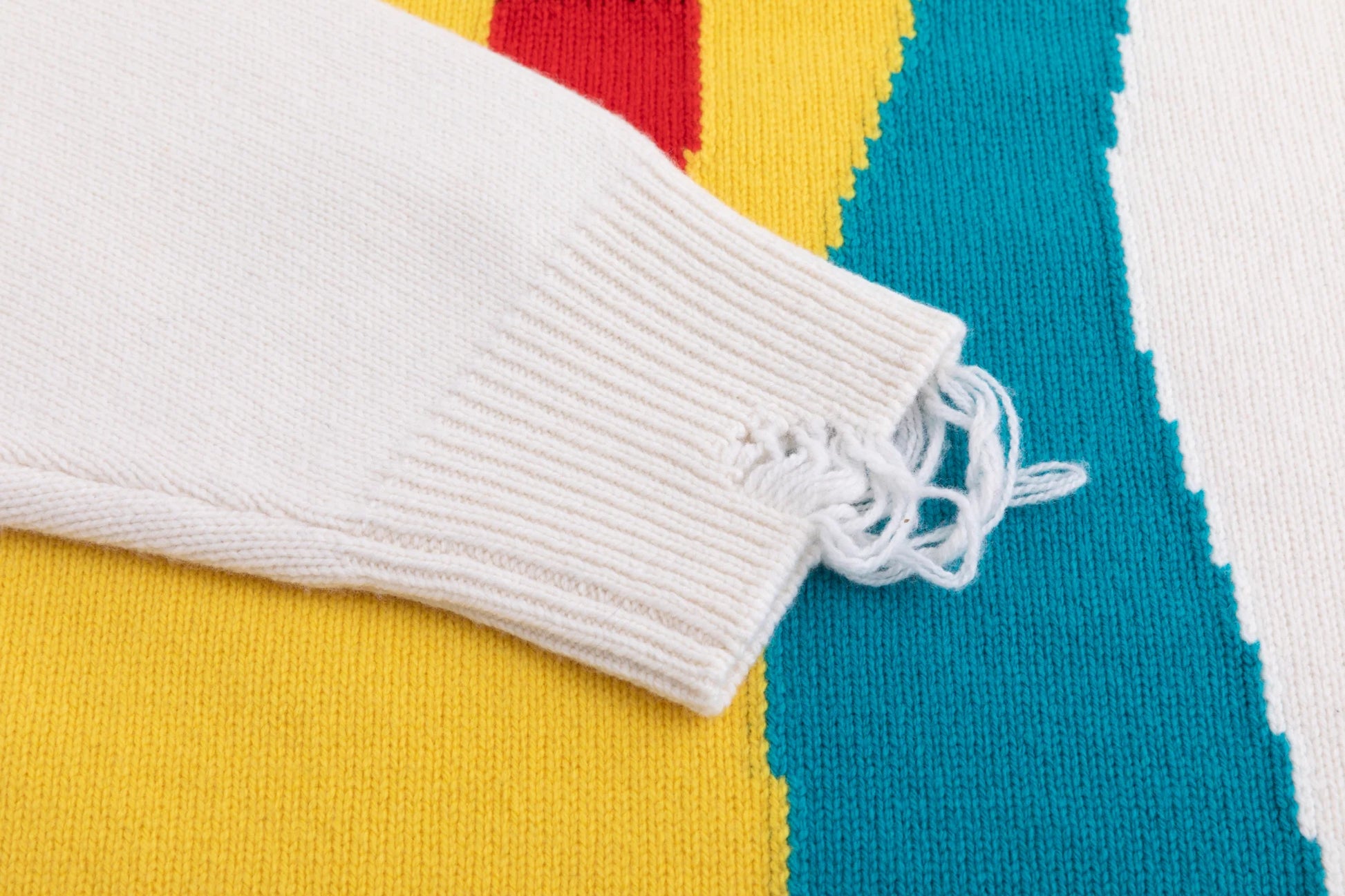 Close-up of the cuff on the ivory jumper with distressed ribbing beside the abstract cat jacquard.