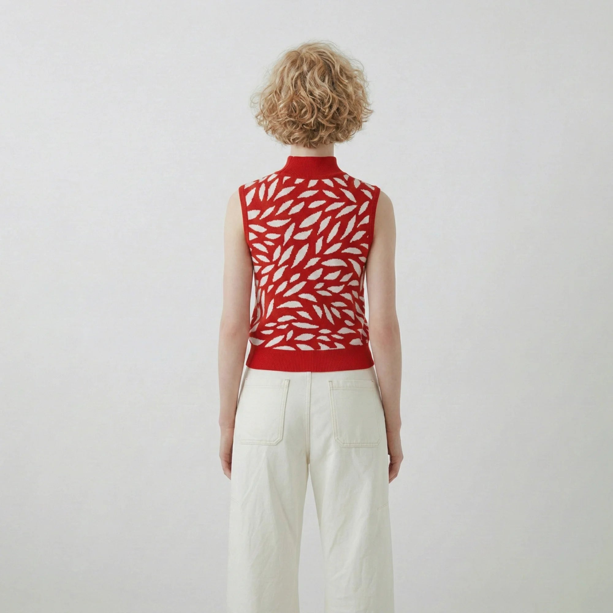 Back view of model wearing a red and white cotton and silk blend knit top with an all-over abstract leaf jacquard and a sleeveless spring summer silhouette.