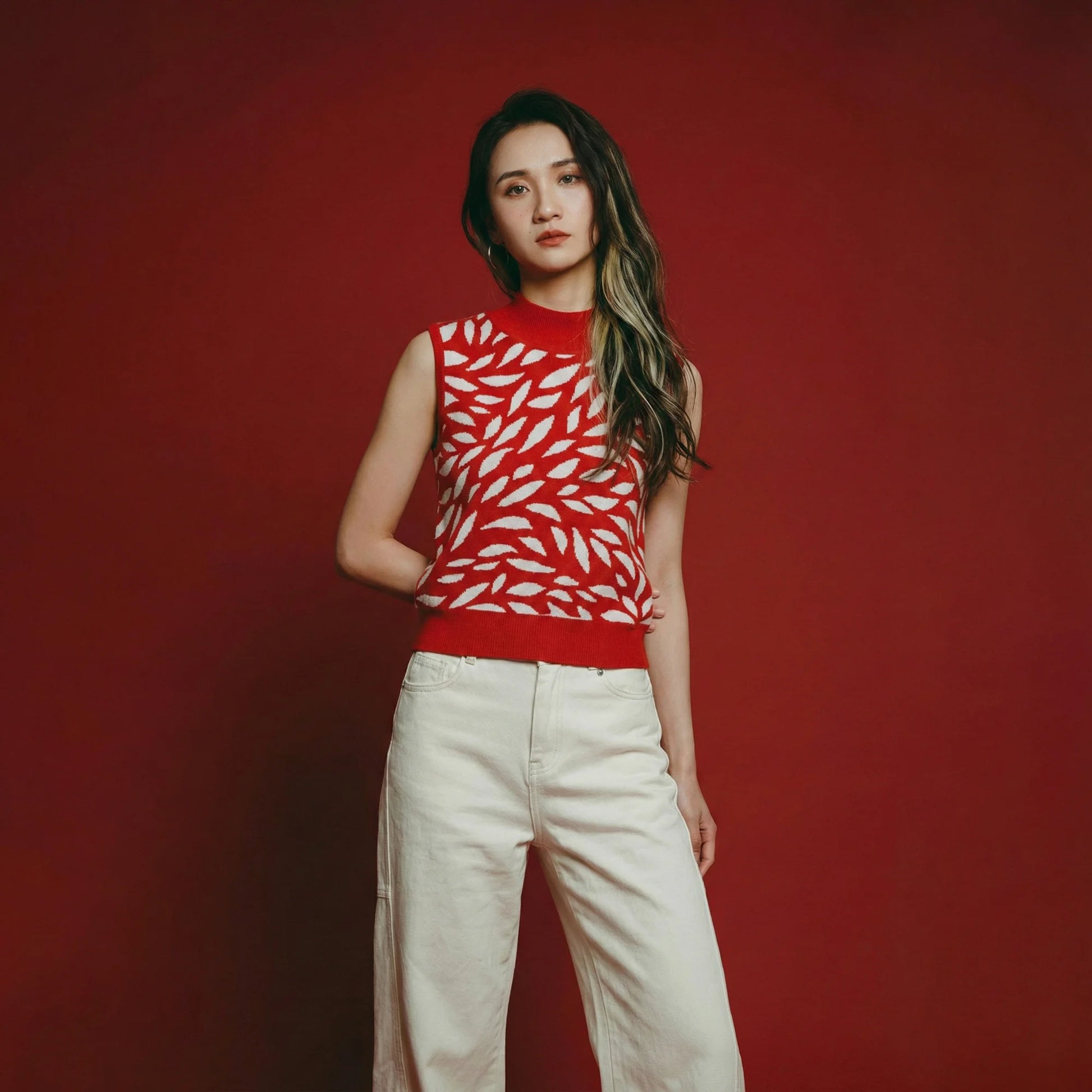 Model in a red sleeveless knit top with white leaf pattern against a red backdrop