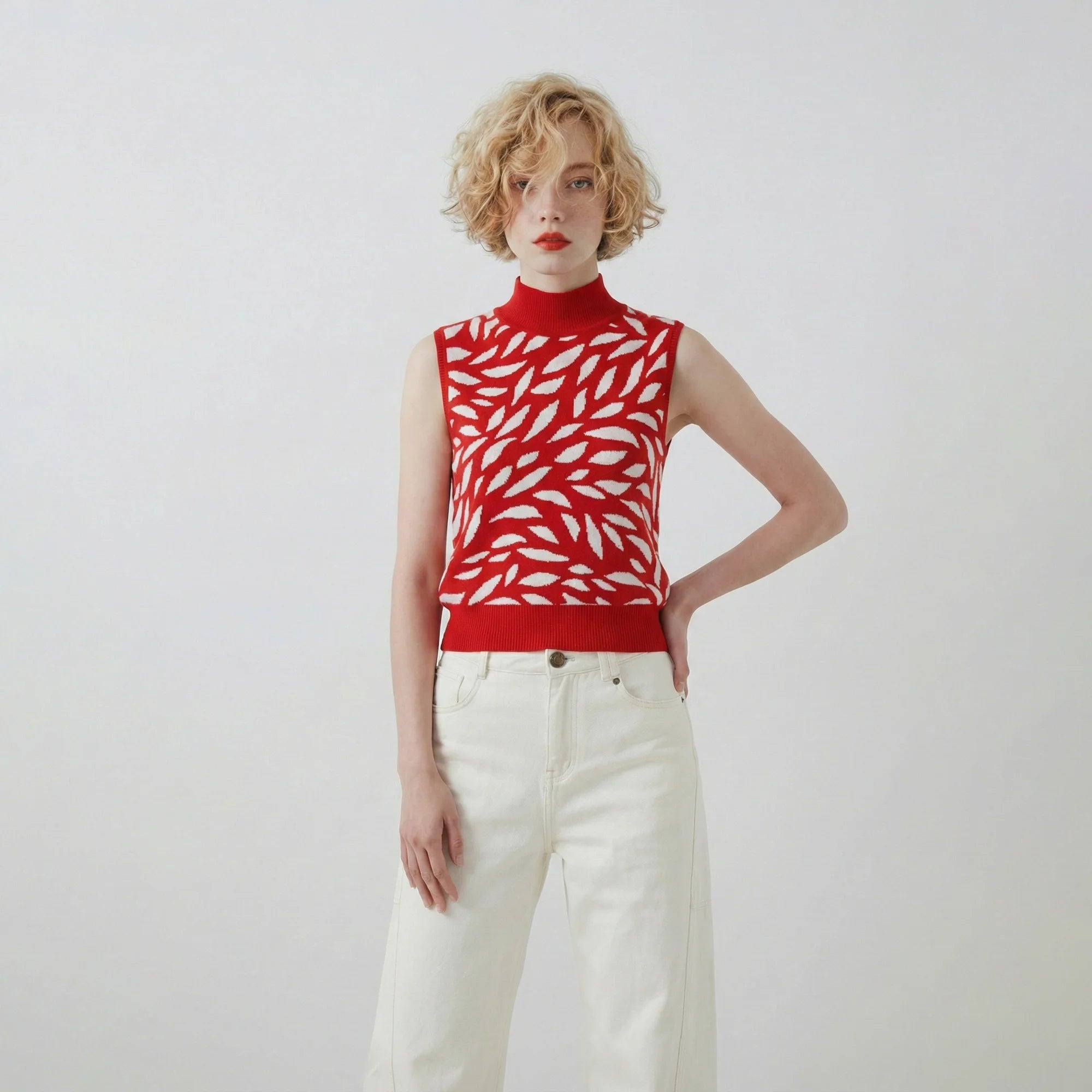 Model wearing a red and white cotton and silk blend knit top with an all-over abstract leaf jacquard and a sleeveless spring summer silhouette.