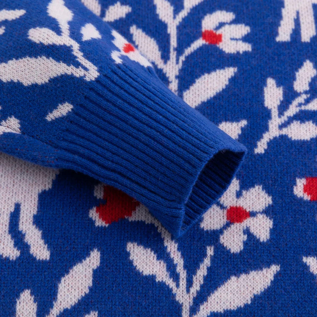 Blue ribbed cuff with white and red floral motifs on the knitted jumper
