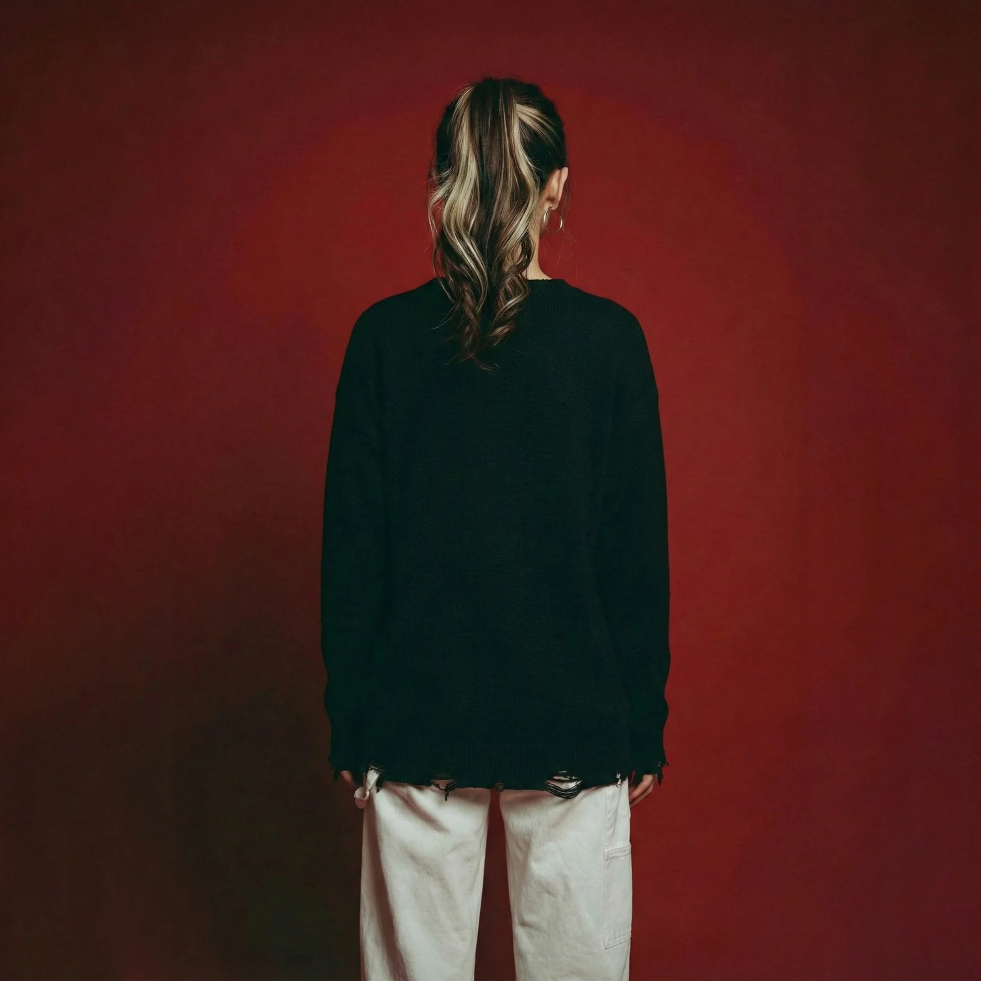 Back view of model wearing a black cotton and wool blend jumper with an oversized dropped-shoulder fit and distressed ribbed hem and cuffs.