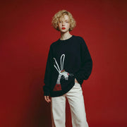 Woman wearing a navy oversized wool jumper with an artistic rabbit embroidery on the front.