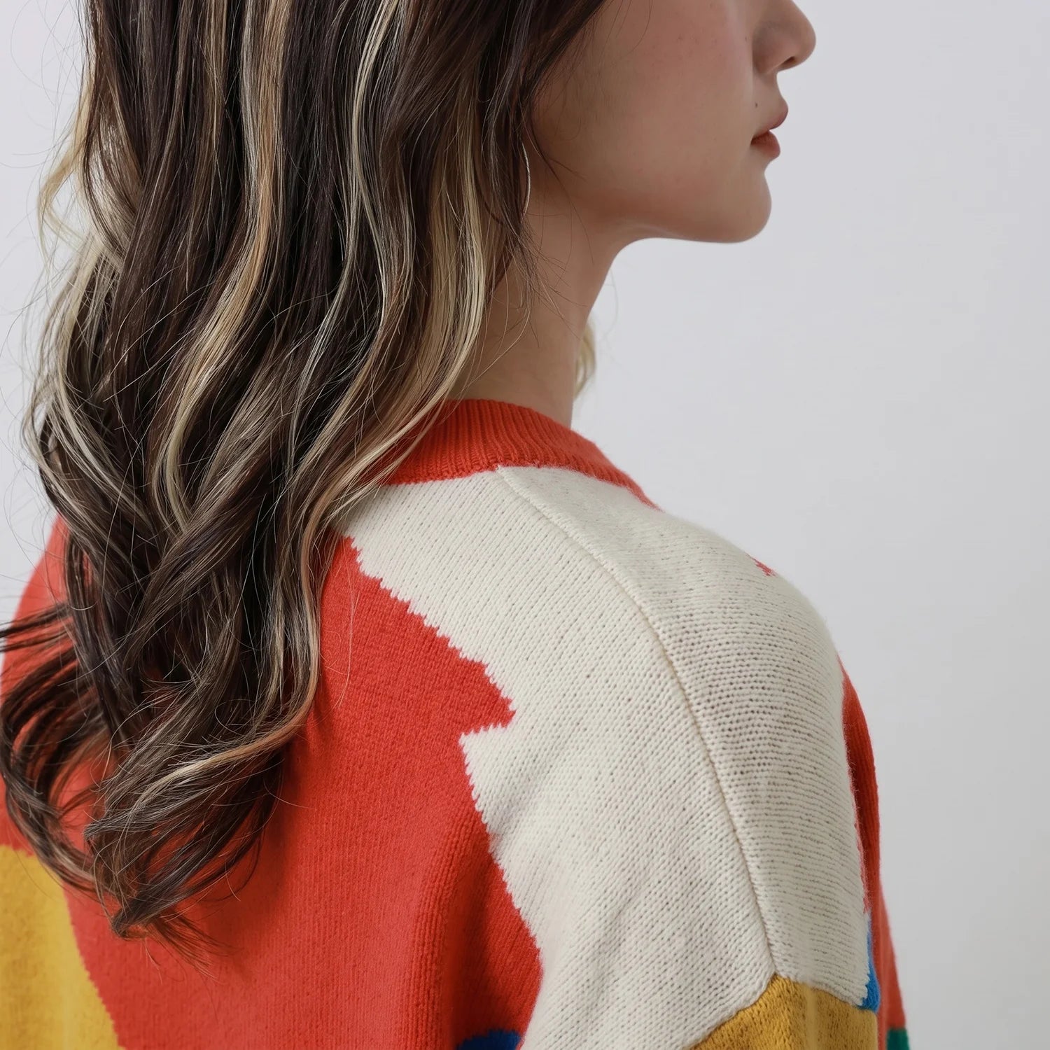 Close-up of the shoulder and neckline on a coral multicolour merino wool jumper.