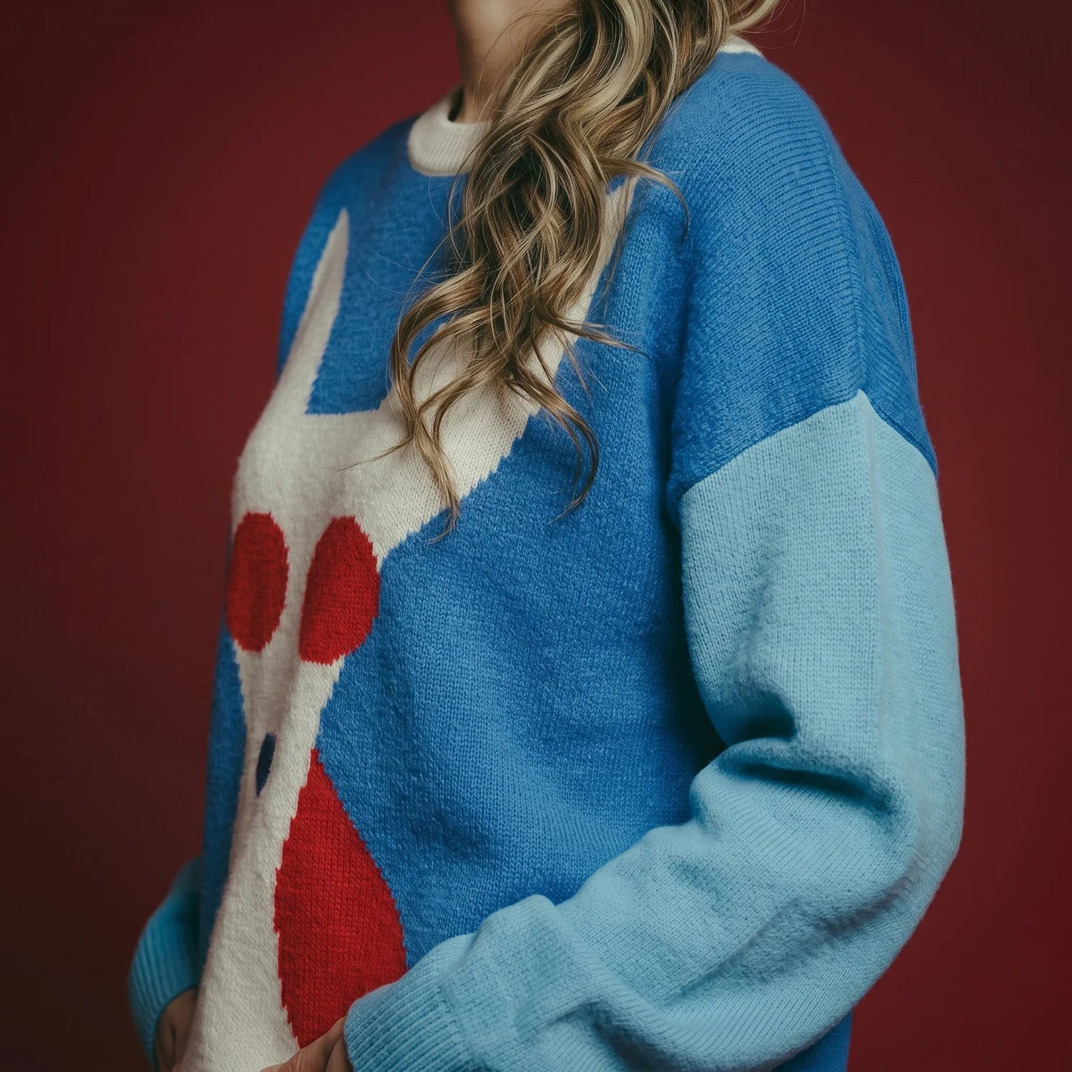 Close-up of a blue merino wool jumper with a white dog and red sunglasses intarsia.