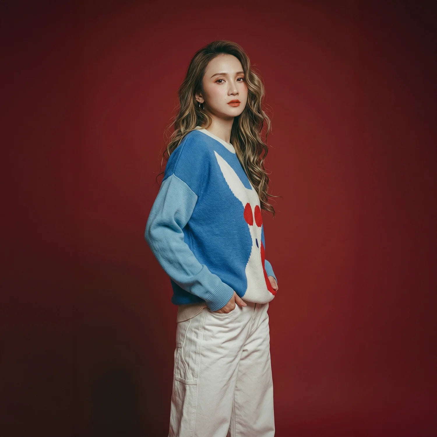 Model wearing a blue merino wool jumper with a white dog and red sunglasses intarsia.