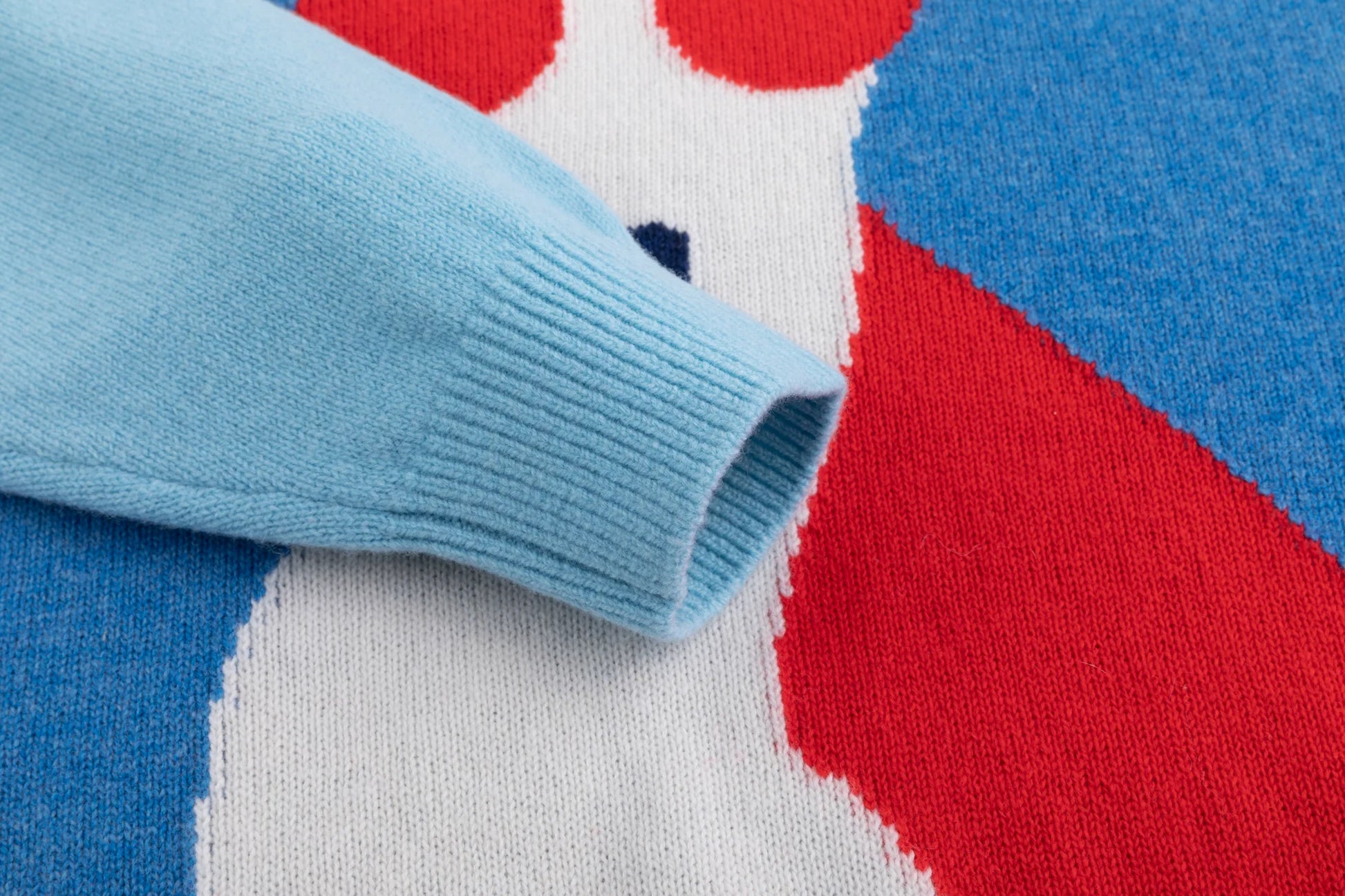 Close-up of the light blue ribbed cuff beside the contrasting dog intarsia on the blue jumper.