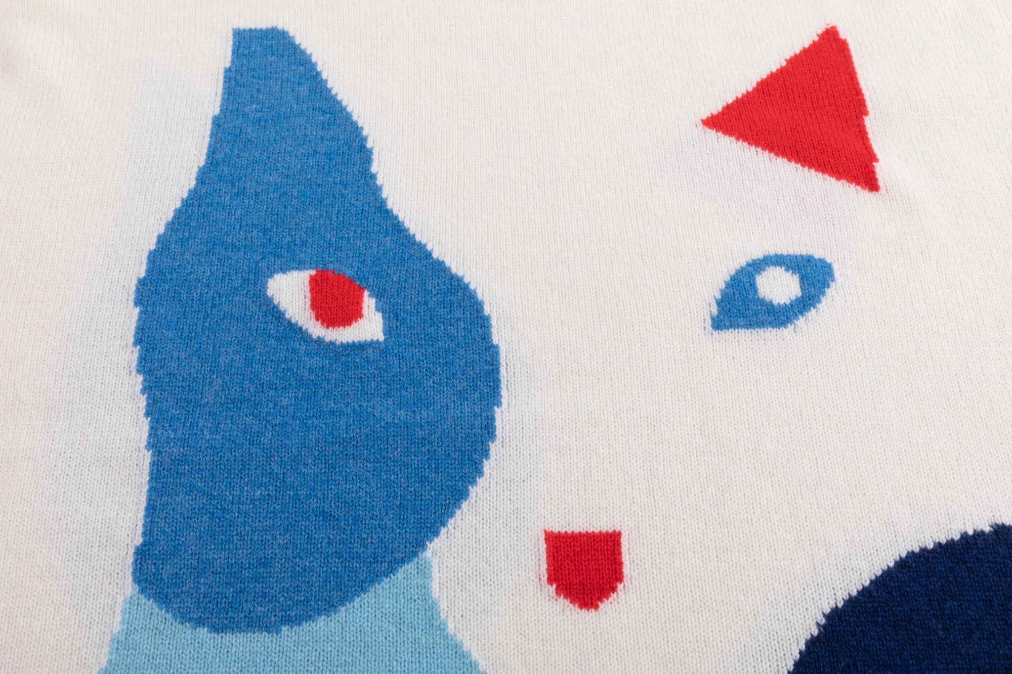 Close-up of the abstract cat intarsia with contrasting blue and red details on the cream jumper.